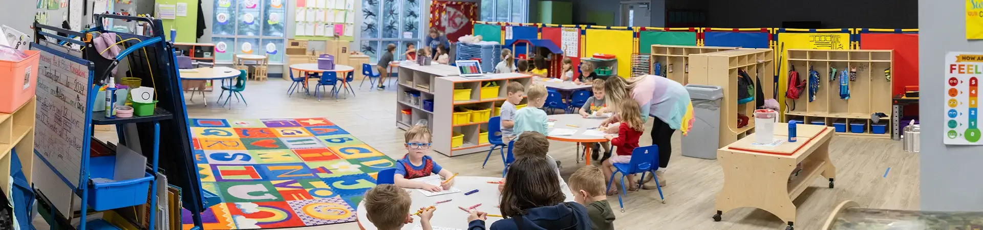 Classroom With Round Tables With Kids And Teachers