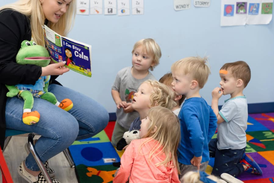 Preschool teacher reading to a group of students sitting on floor.