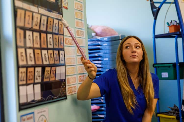 Preschool teacher pointing at calendar instruction tool.