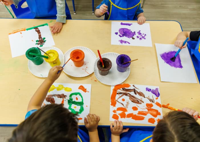Preschoolers wearing blue smocks painting at a table.