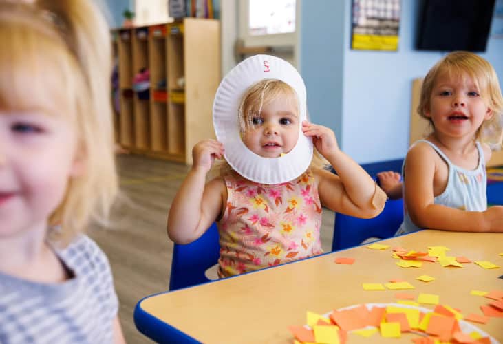 Three preschoolers sitting at a table doing a fall craft activity.